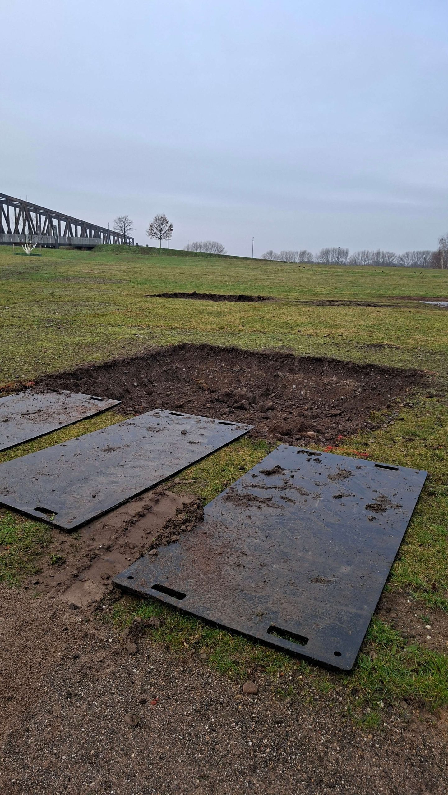 Ausgehobene Pflanzgrube für einen neuen Baum auf einer Wiese im RheinPark, daneben schwarze Fahrplatten.