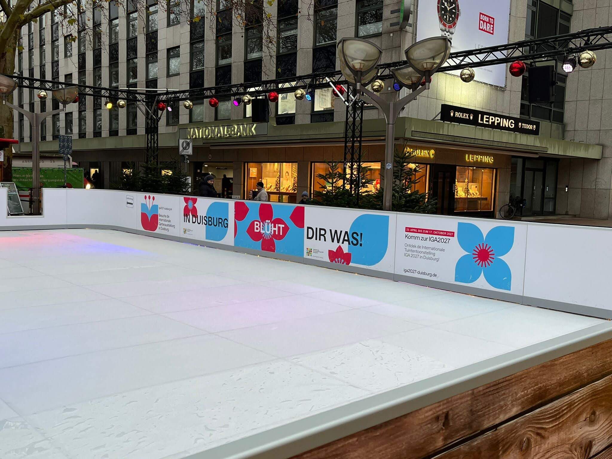 Eislaufende vor einer Bande mit IGA-Werbung und dem Schriftzug In Duisburg blüht dir was auf einer Eisbahn am Weihnachtsmarkt.