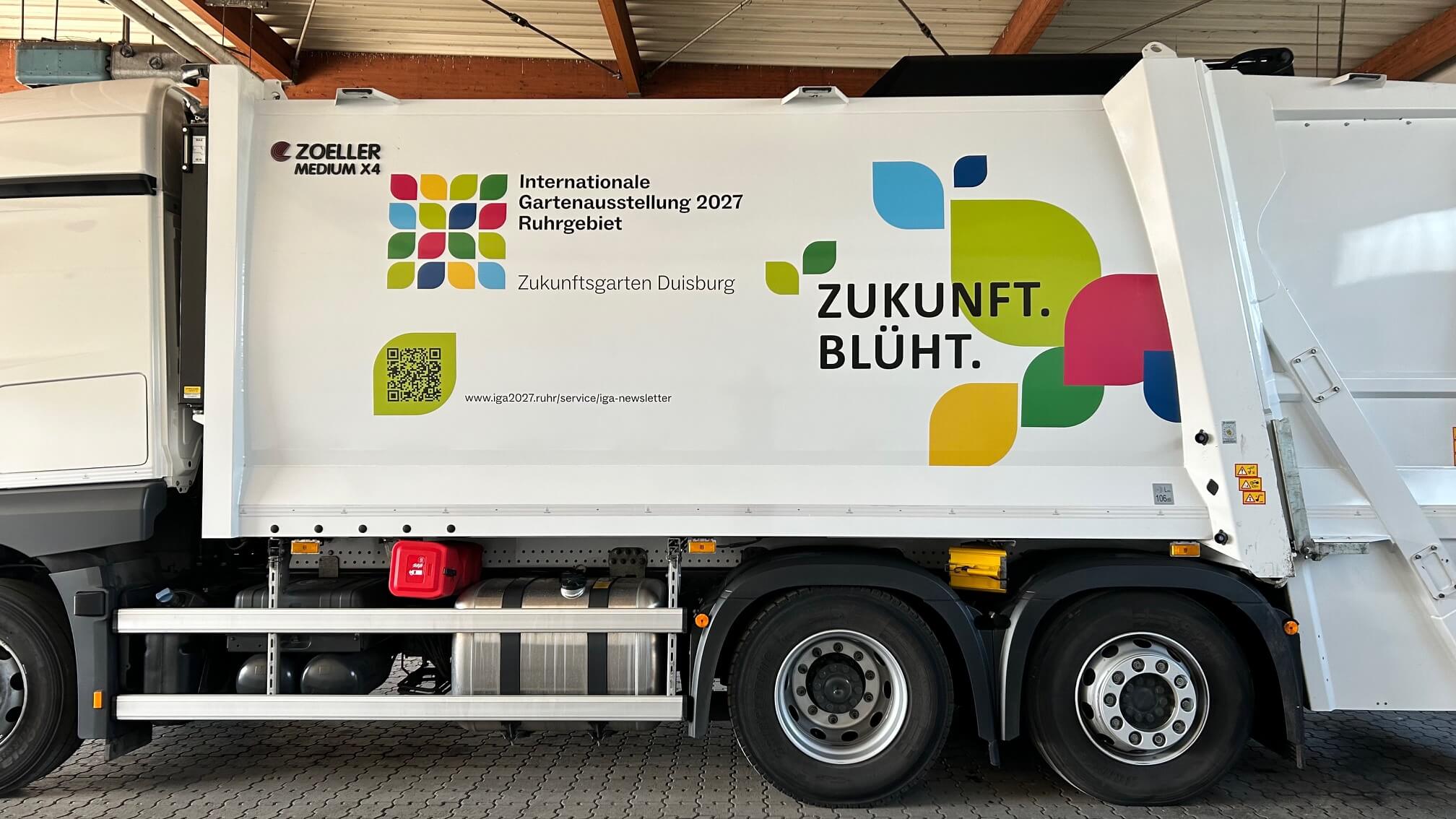 Weißes Abfallfahrzeuge der Wirtschaftsbetriebe Duisburg trägt eine Beklebung im IGA-Design: Logo, bunte Blättergrafik, QR-Code und die Aufschrift „Zukunft. Blüht.“
