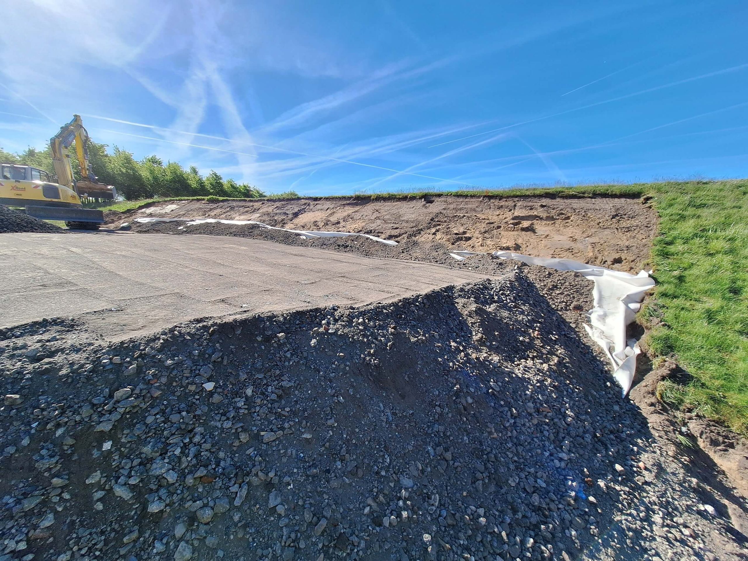 Vorbereitete Schotterfläche mit Geotextil an einer Böschung, links ein Bagger.
