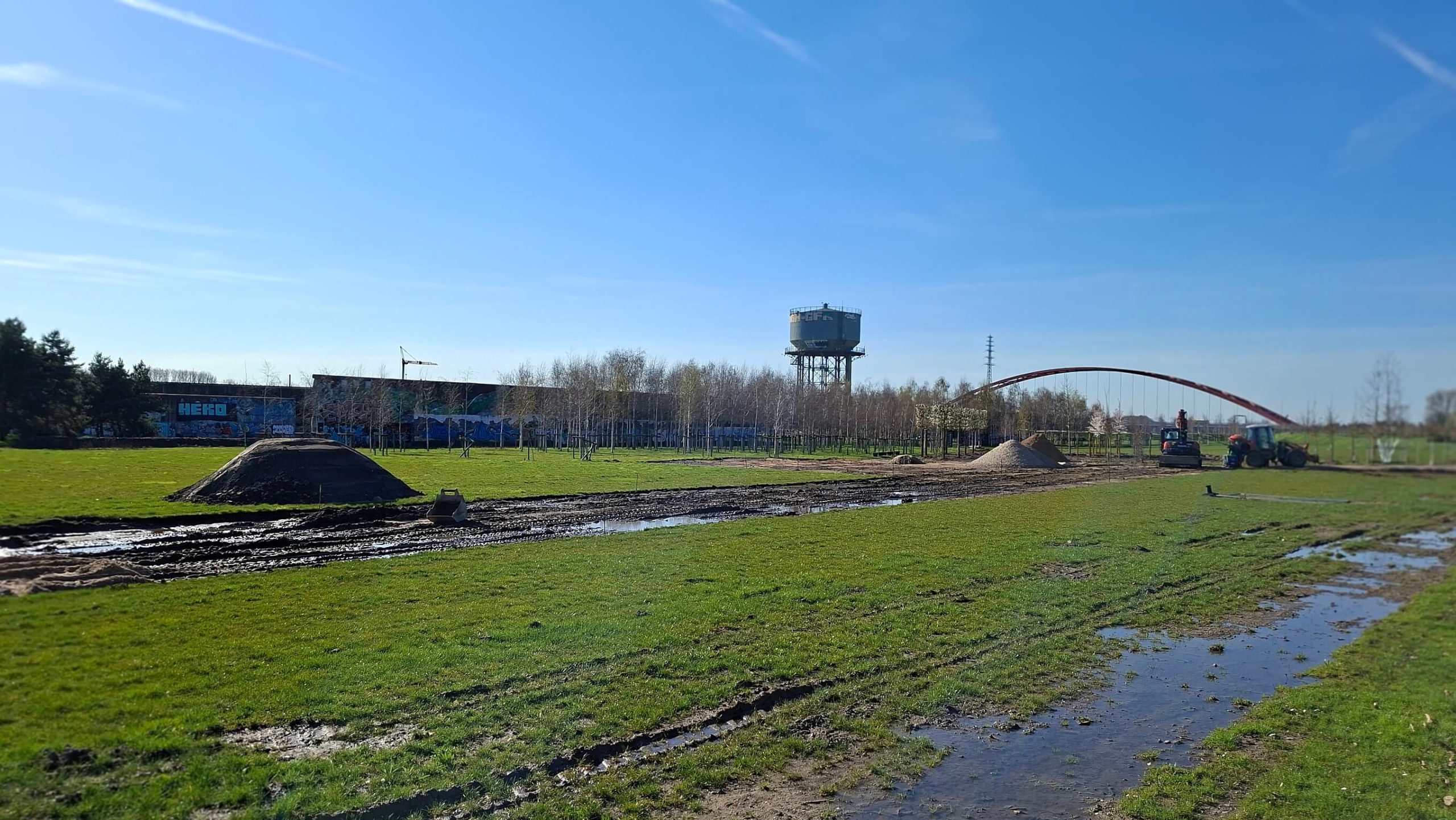Bewässerungsarbeiten im RheinPark: Rohrleitung wird über eine Wiese verlegt, im Hintergrund der Wasserturm und die Bunkerwand.