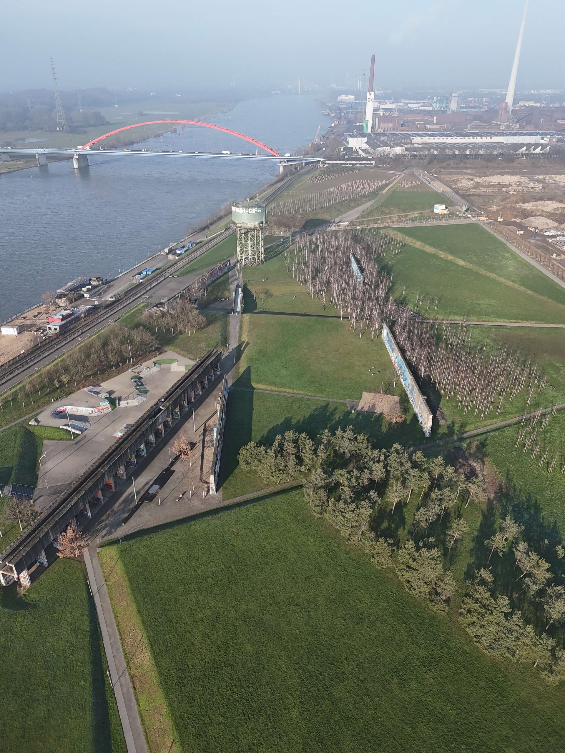 Luftaufnahme des RheinParks im Winter: Wasserturm, Skateanlage, Bunkerwände und Birkenwäldchen am Rheinufer.
