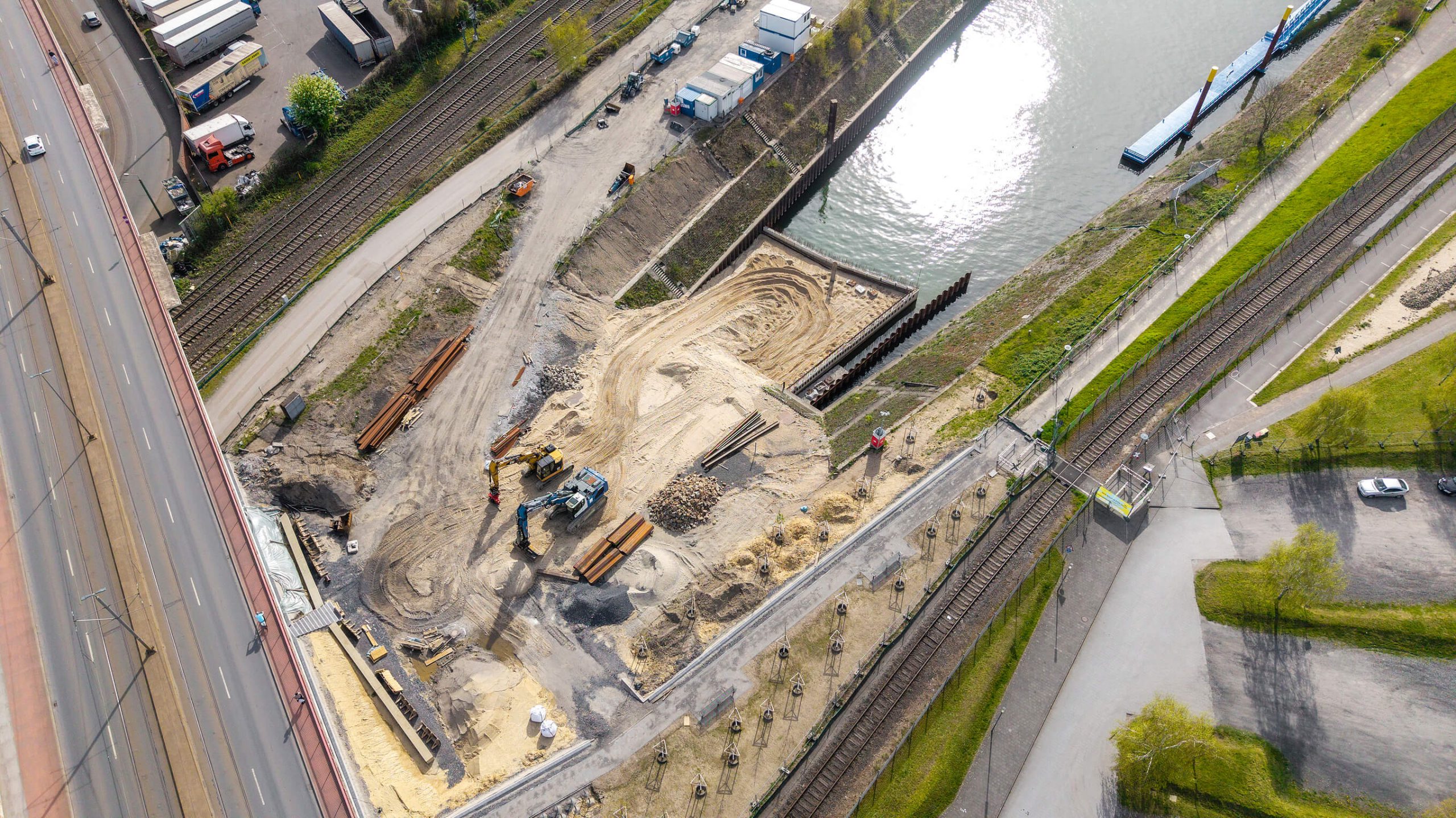 Luftaufnahme der Baustelle am Kultushafen von oben: Bagger und Erdarbeiten zwischen Hochstraße, Bahngleisen und dem Hafenbecken mit blauem Anleger.