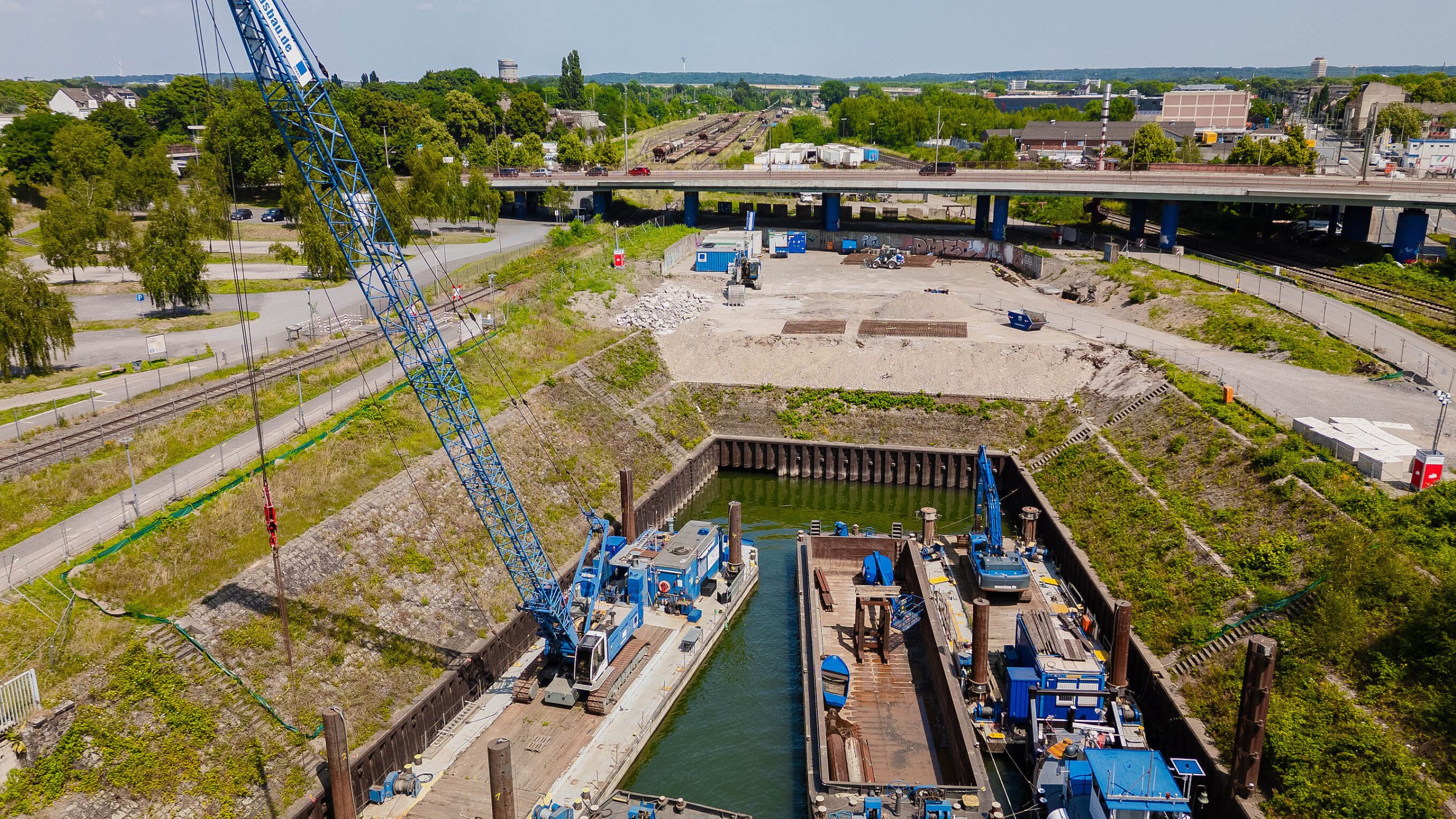 Zwei Arbeitspontons mit blauen Kranen im Hafenbecken am Kultushafen, dahinter die verfüllte Fläche und die Hochstraße.