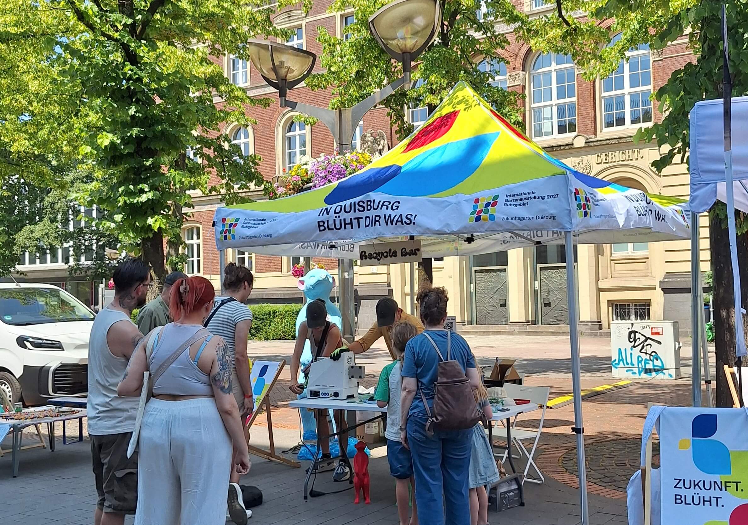 Mehrere Menschen stehen an einem Pavillon im IGA-Design und verfolgen aufmerksam das Workshop-Angebot „Ausgedient? Umgedacht“.