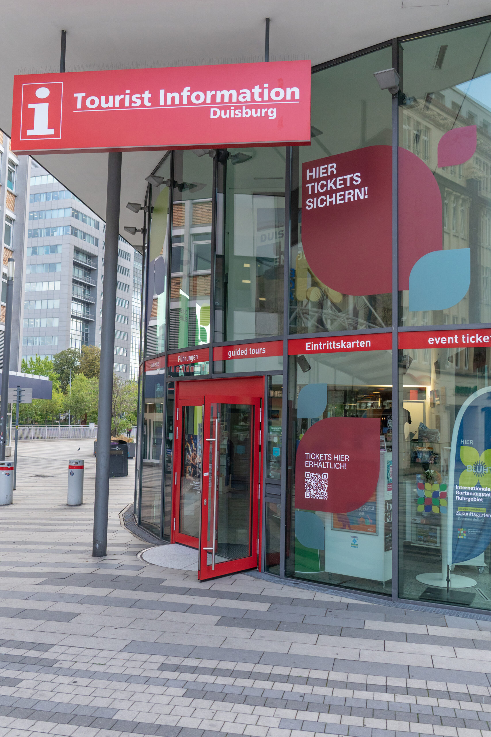 Das Gebäude der Duisburger Touristeninformation in der Innenstadt ist großflächig mit dem IGA-Design beklebt. Die Fensterfront ist mit bunten Blütenblatt-Motiven und einem QR-Code für das Ticketangebot der IGA 2027 gestaltet.