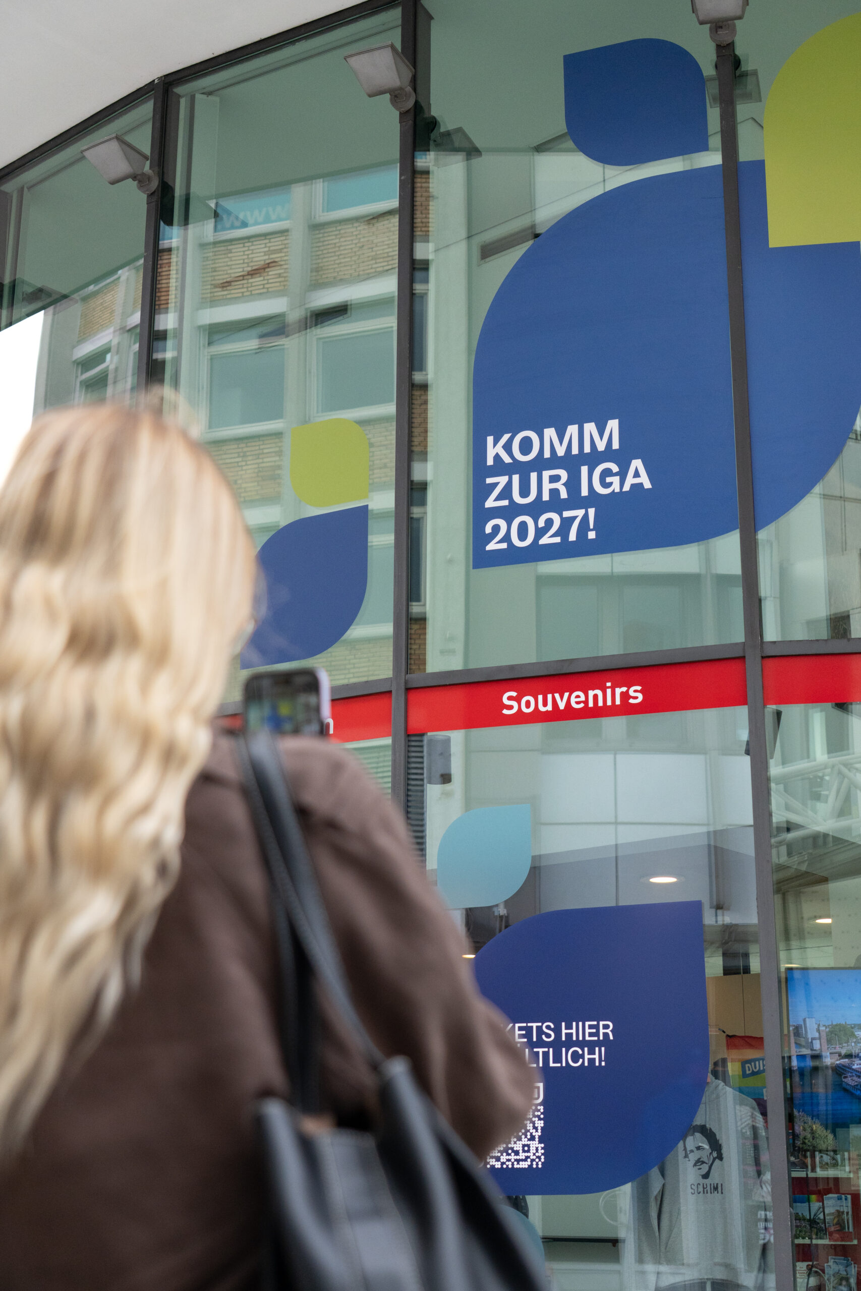 Das Gebäude der Duisburger Touristeninformation in der Innenstadt ist großflächig mit dem IGA-Design beklebt. Die Fensterfront ist mit bunten Blütenblatt-Motiven und einem QR-Code für das Ticketangebot der IGA 2027 gestaltet.